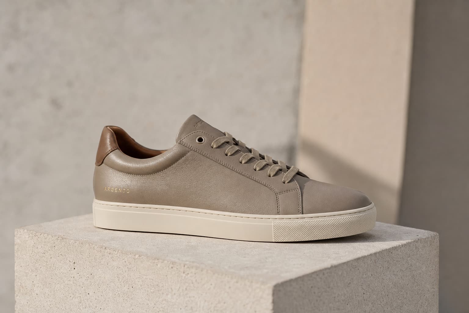 Une sneaker minimaliste en cuir reposant sur un bloc de béton sous une lumière naturelle douce.