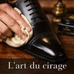 Gros plan d'une chaussure en cuir élégante polie avec un chiffon doux sur une table en bois, texte 'L'art du cirage' superposé en bas.