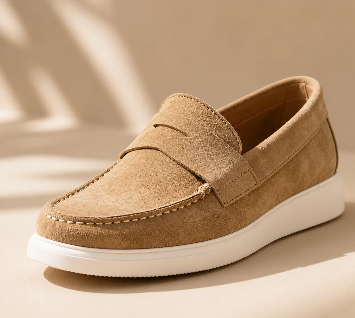 Gros plan d'un mocassin en cuir velours couleur sable, posé sur un fond neutre, avec une lumière douce révélant la texture veloutée.
